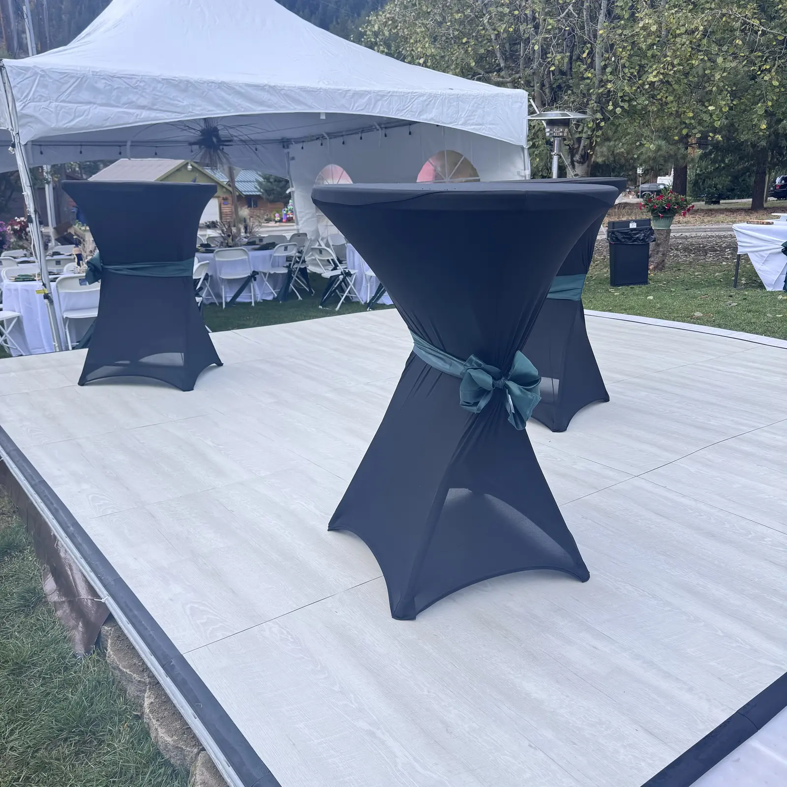 Black-covered cocktail tables with green bows on a white dance floor near a white tent