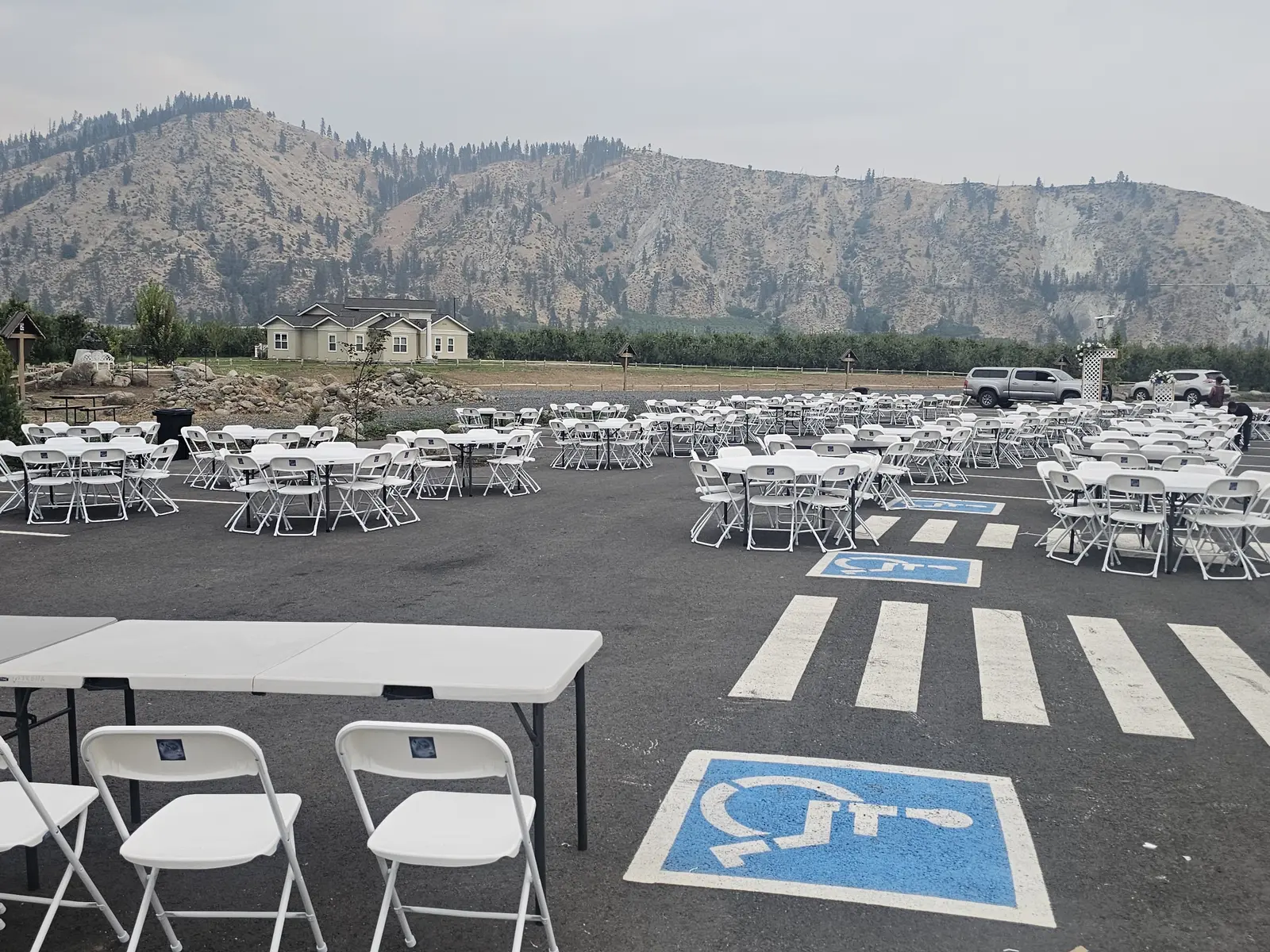 Outdoor event setup with rows of white chairs and tables against mountains
