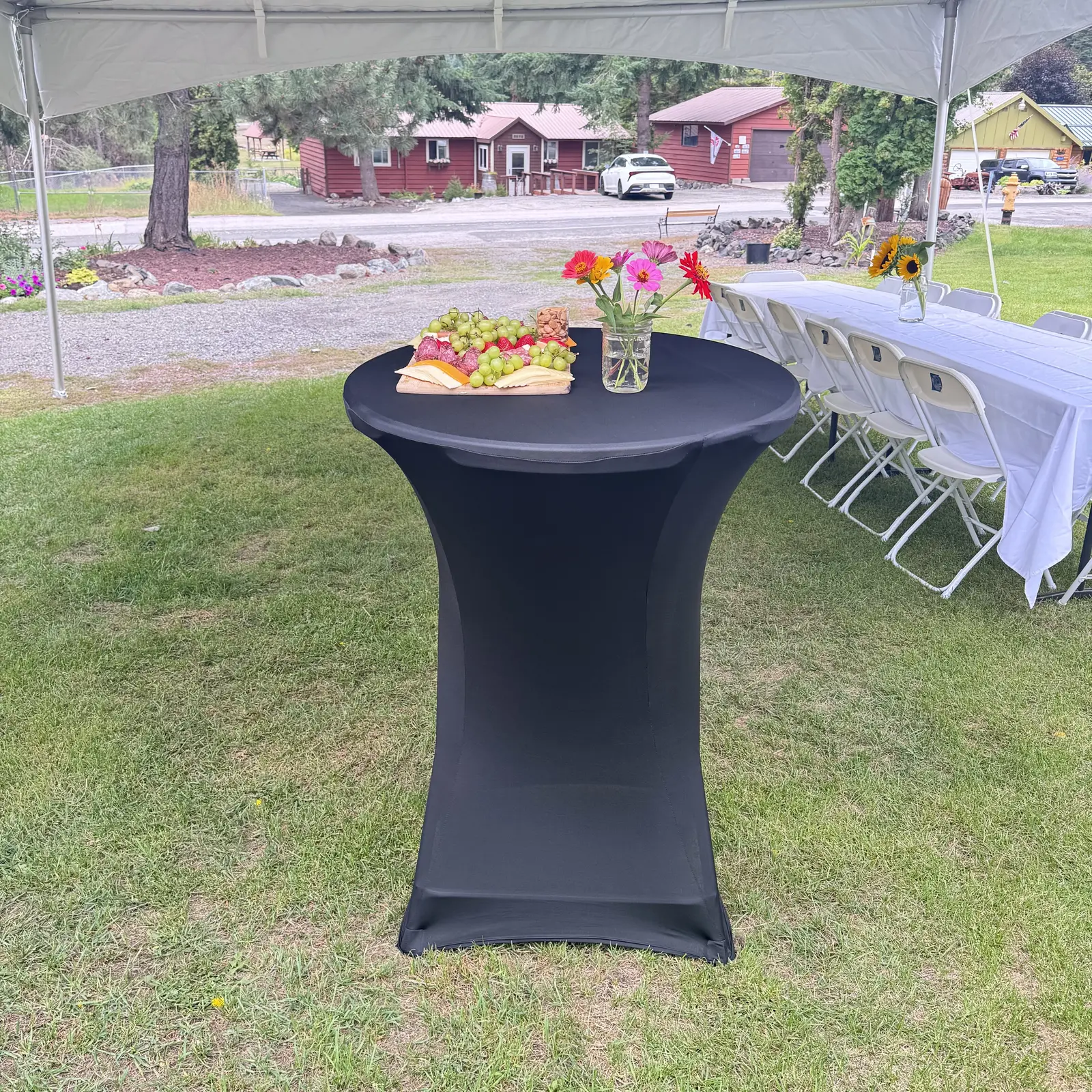 A black cocktail table with flowers beside white-covered tables
